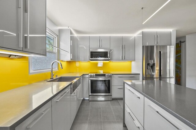 kitchen featuring tile patterned flooring, gray cabinets, a sink, appliances with stainless steel finishes, and backsplash