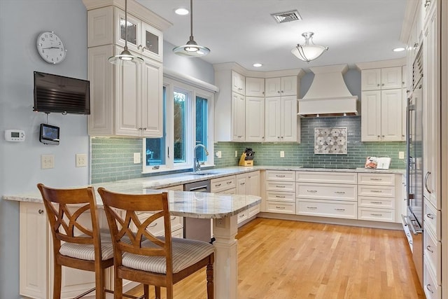 kitchen with kitchen peninsula, custom exhaust hood, pendant lighting, a kitchen breakfast bar, and sink