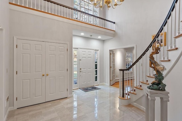 foyer featuring a towering ceiling, baseboard heating, a notable chandelier, and a wealth of natural light