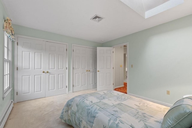 carpeted bedroom with a baseboard radiator, multiple closets, and a skylight