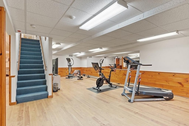 exercise area with a paneled ceiling, wood walls, and hardwood / wood-style floors