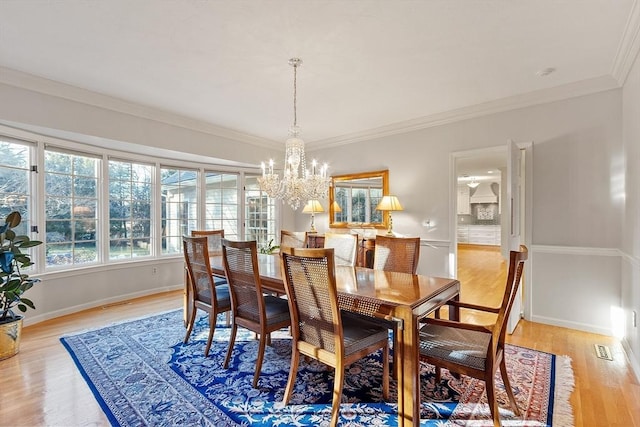 dining room with ornamental molding, a notable chandelier, and light hardwood / wood-style flooring