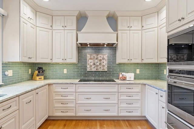 kitchen featuring light stone counters, premium range hood, black electric stovetop, backsplash, and stainless steel double oven