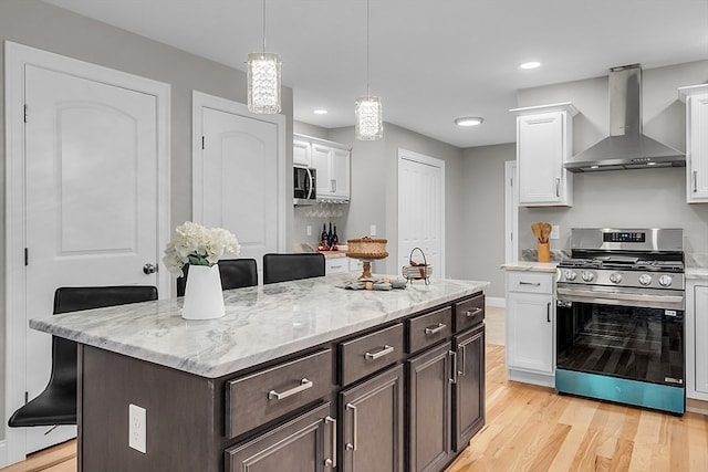 kitchen with appliances with stainless steel finishes, a kitchen bar, wall chimney range hood, and white cabinetry