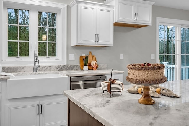 kitchen featuring white cabinets, sink, stainless steel dishwasher, and light stone counters