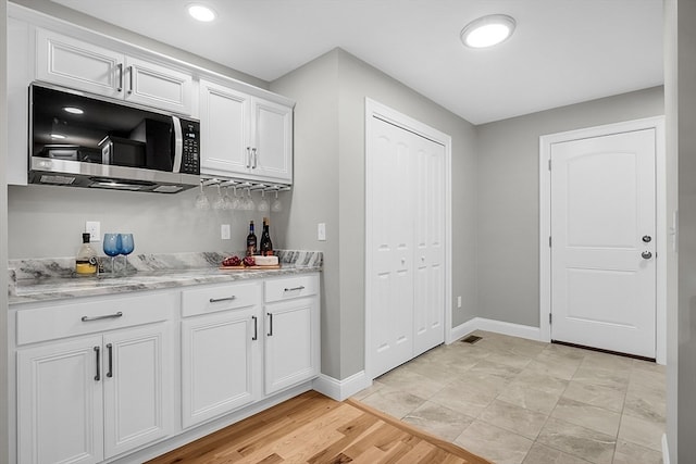 bar featuring light stone countertops, light hardwood / wood-style flooring, and white cabinets