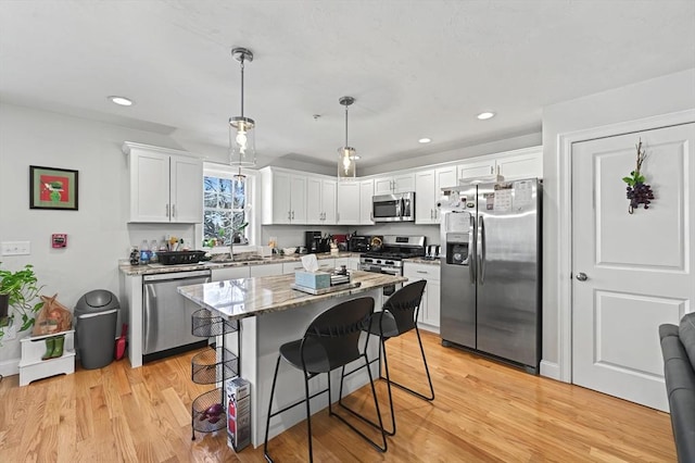 kitchen with white cabinetry, decorative light fixtures, a kitchen breakfast bar, a kitchen island, and stainless steel appliances