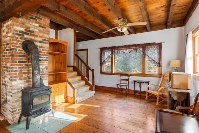 sitting room featuring beamed ceiling, wood ceiling, a wood stove, and light hardwood / wood-style flooring