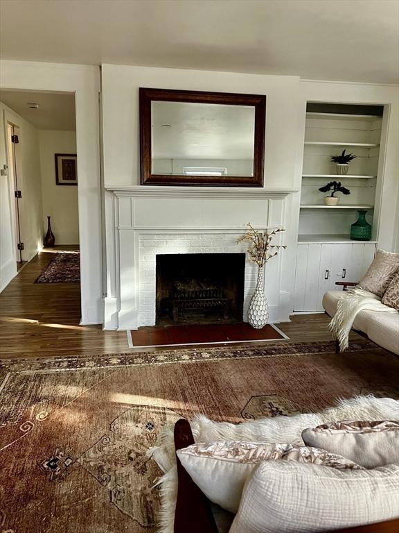 living room featuring a tile fireplace, wood-type flooring, and built in shelves