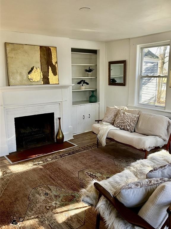 living room with built in shelves, hardwood / wood-style floors, and a brick fireplace