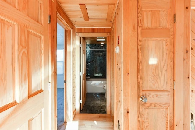 hallway featuring light wood-type flooring, wooden ceiling, and wood walls