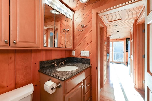 bathroom with vanity, wooden ceiling, wooden walls, toilet, and wood-type flooring