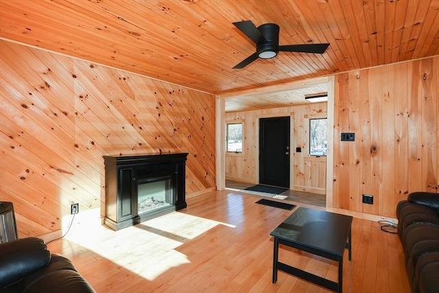 living room with ceiling fan, wooden walls, wooden ceiling, and light wood-type flooring