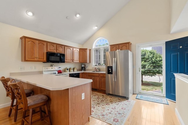 905 Village Ln Unit 905, Bellingham, MA 02019 - kitchen with black appliances, a peninsula, a kitchen breakfast bar, high vaulted ceiling, and light wood-style floors