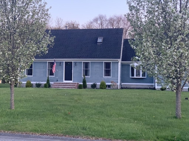 new england style home with entry steps, roof with shingles, and a front lawn