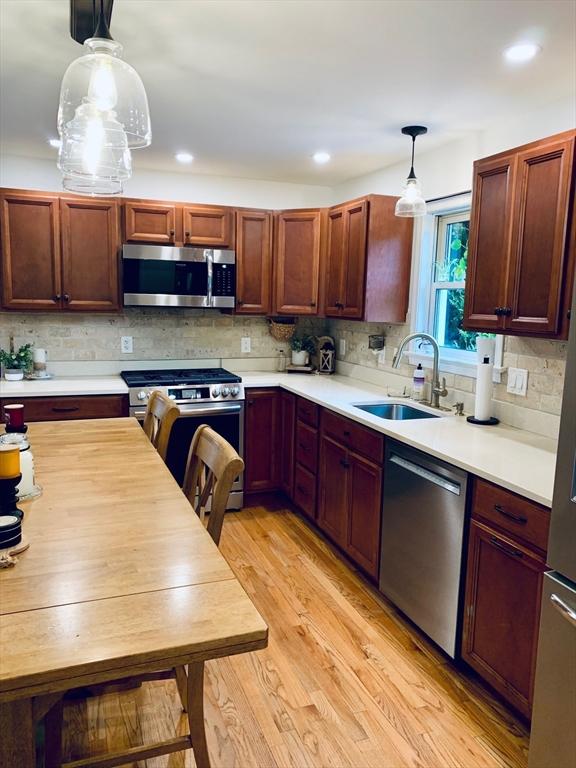 kitchen with hanging light fixtures, a sink, light countertops, appliances with stainless steel finishes, and decorative backsplash