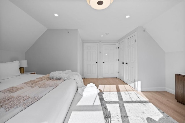 bedroom with vaulted ceiling, multiple closets, and light wood-type flooring