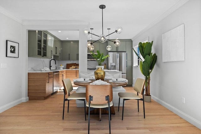 dining room with ornamental molding, sink, an inviting chandelier, and light hardwood / wood-style flooring