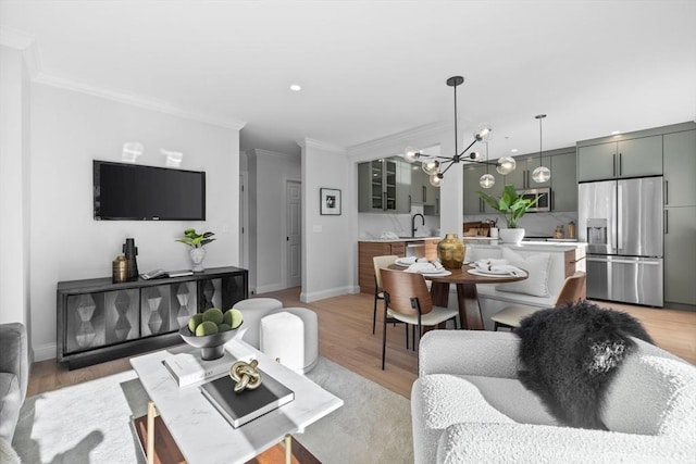 living room with ornamental molding, sink, a notable chandelier, and light hardwood / wood-style flooring