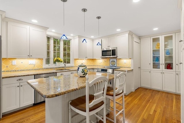 8 Warren Rd, Marblehead, MA 01945 - kitchen featuring appliances with stainless steel finishes, light wood-style flooring, a breakfast bar area, a center island, and white cabinetry