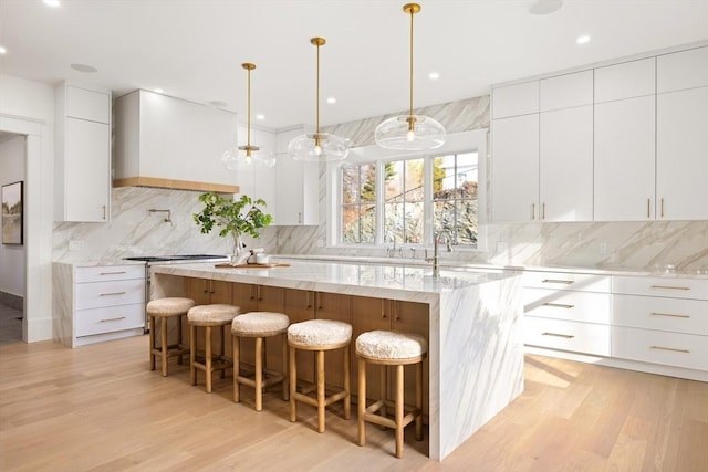 kitchen featuring white cabinets, decorative light fixtures, and an island with sink