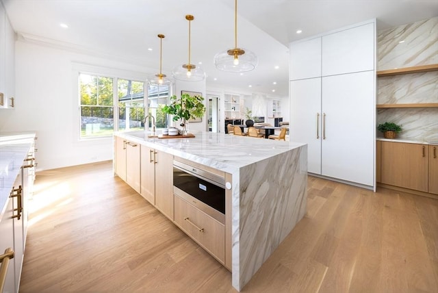 kitchen featuring pendant lighting, a center island with sink, white cabinets, light stone countertops, and light hardwood / wood-style floors