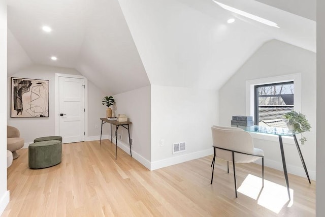 office area with light wood finished floors, visible vents, vaulted ceiling with skylight, and baseboards