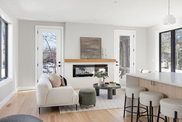 living area with a wealth of natural light, a glass covered fireplace, light wood finished floors, and visible vents