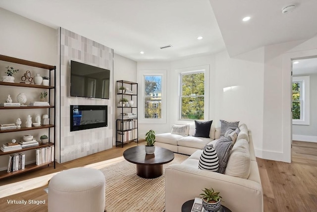 living area featuring a wealth of natural light, a fireplace, visible vents, and wood finished floors