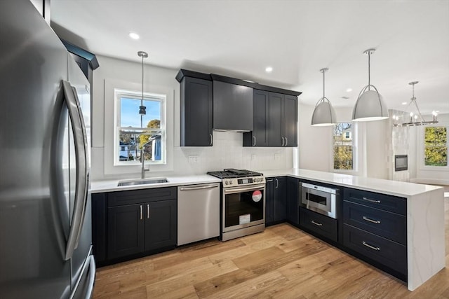 kitchen featuring stainless steel appliances, a peninsula, a sink, a healthy amount of sunlight, and light wood finished floors