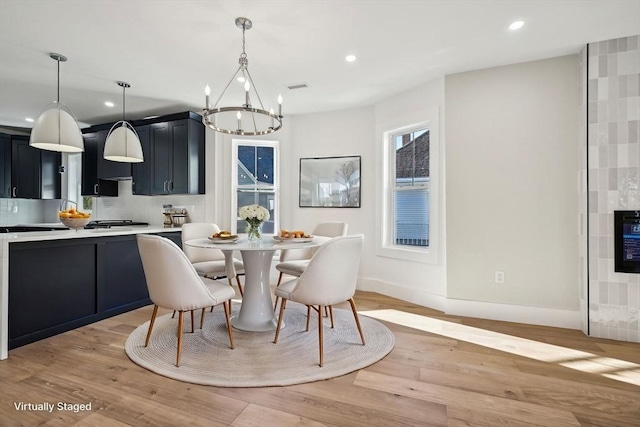 dining space featuring a tiled fireplace, a chandelier, and light hardwood / wood-style flooring