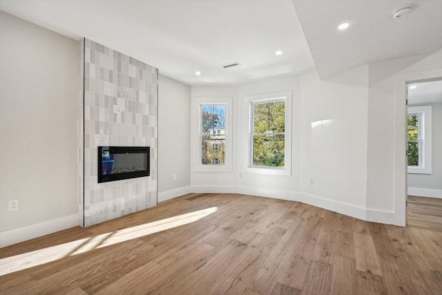 unfurnished living room with a tiled fireplace and light hardwood / wood-style floors