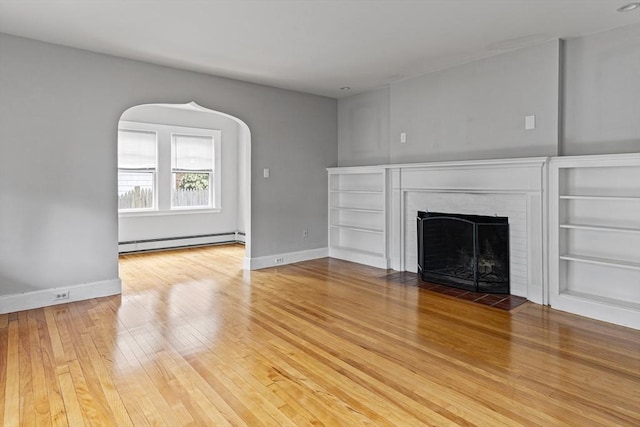 17-19 Maple St, Newton, MA 02466 - unfurnished living room with a baseboard heating unit, a brick fireplace, wood-type flooring, arched walkways, and baseboards