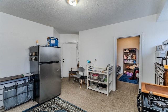 kitchen featuring gas range oven, a textured ceiling, and stainless steel refrigerator