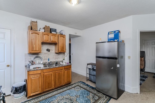 kitchen with sink, decorative backsplash, a textured ceiling, and stainless steel fridge