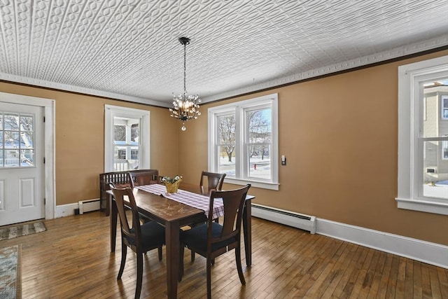 dining space with a baseboard radiator, ornamental molding, hardwood / wood-style floors, and an inviting chandelier