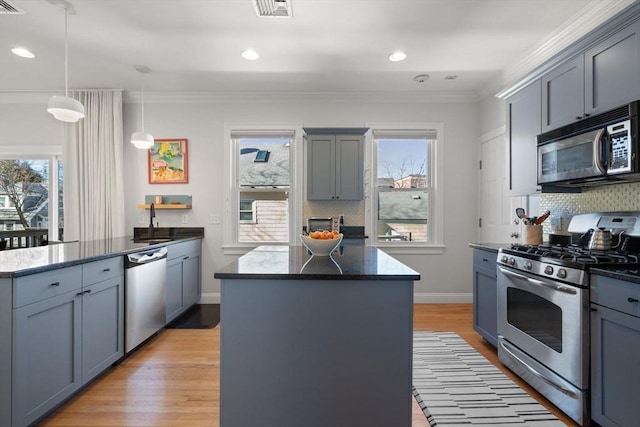 kitchen with appliances with stainless steel finishes, a center island, light wood-type flooring, and decorative light fixtures