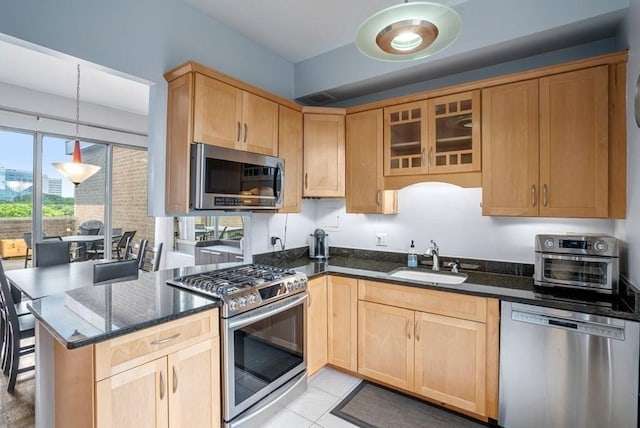 kitchen featuring stainless steel appliances, a sink, light brown cabinetry, dark stone countertops, and a peninsula