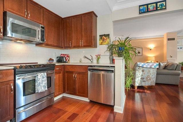 kitchen featuring dark wood-style floors, ornamental molding, stainless steel appliances, light countertops, and backsplash