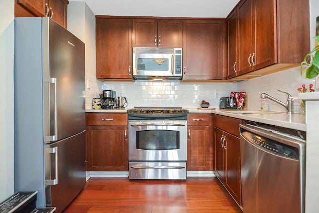 kitchen featuring decorative backsplash, appliances with stainless steel finishes, dark wood-type flooring, light countertops, and a sink