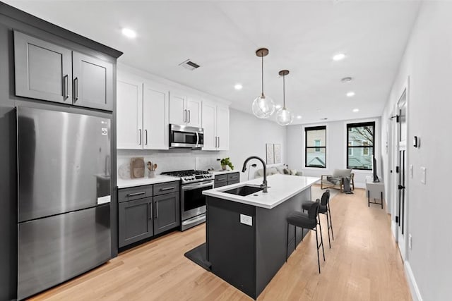 kitchen featuring backsplash, stainless steel appliances, light wood-style floors, and a sink