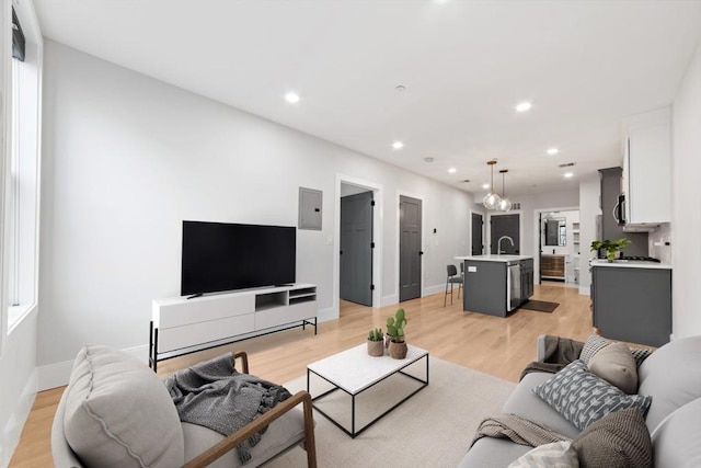 living area featuring electric panel, recessed lighting, light wood-type flooring, and baseboards