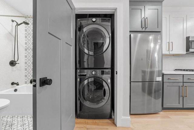 clothes washing area featuring stacked washer / drying machine, light wood-style flooring, and laundry area