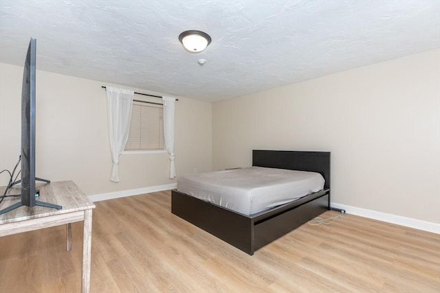 bedroom with baseboards, a textured ceiling, and light wood-style flooring