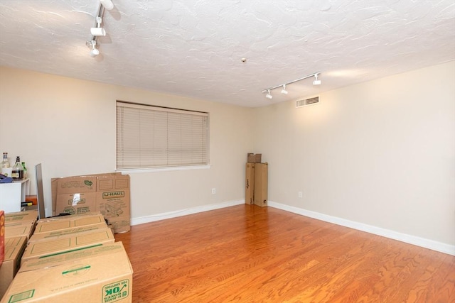 basement featuring a textured ceiling, rail lighting, visible vents, and light wood-type flooring