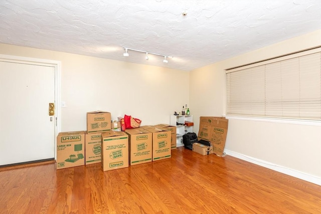 misc room with baseboards, rail lighting, a textured ceiling, and wood finished floors