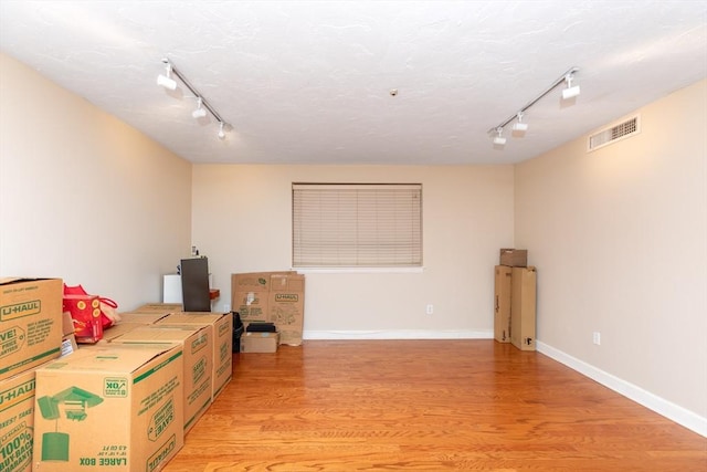 below grade area with visible vents, rail lighting, light wood finished floors, and baseboards