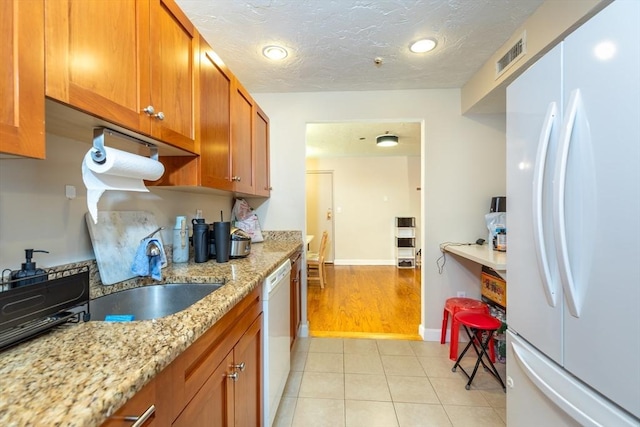 kitchen featuring a sink, white appliances, brown cabinetry, baseboards, and visible vents