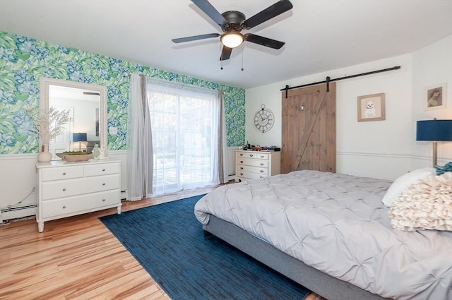 bedroom with light wood-type flooring, a baseboard radiator, ceiling fan, and a barn door