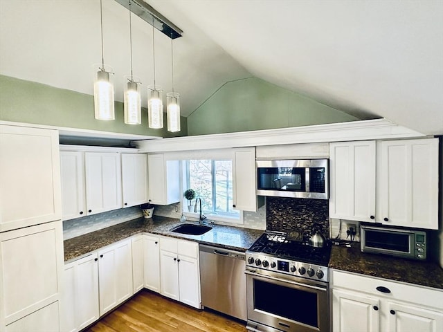 kitchen featuring appliances with stainless steel finishes, vaulted ceiling, sink, pendant lighting, and white cabinetry